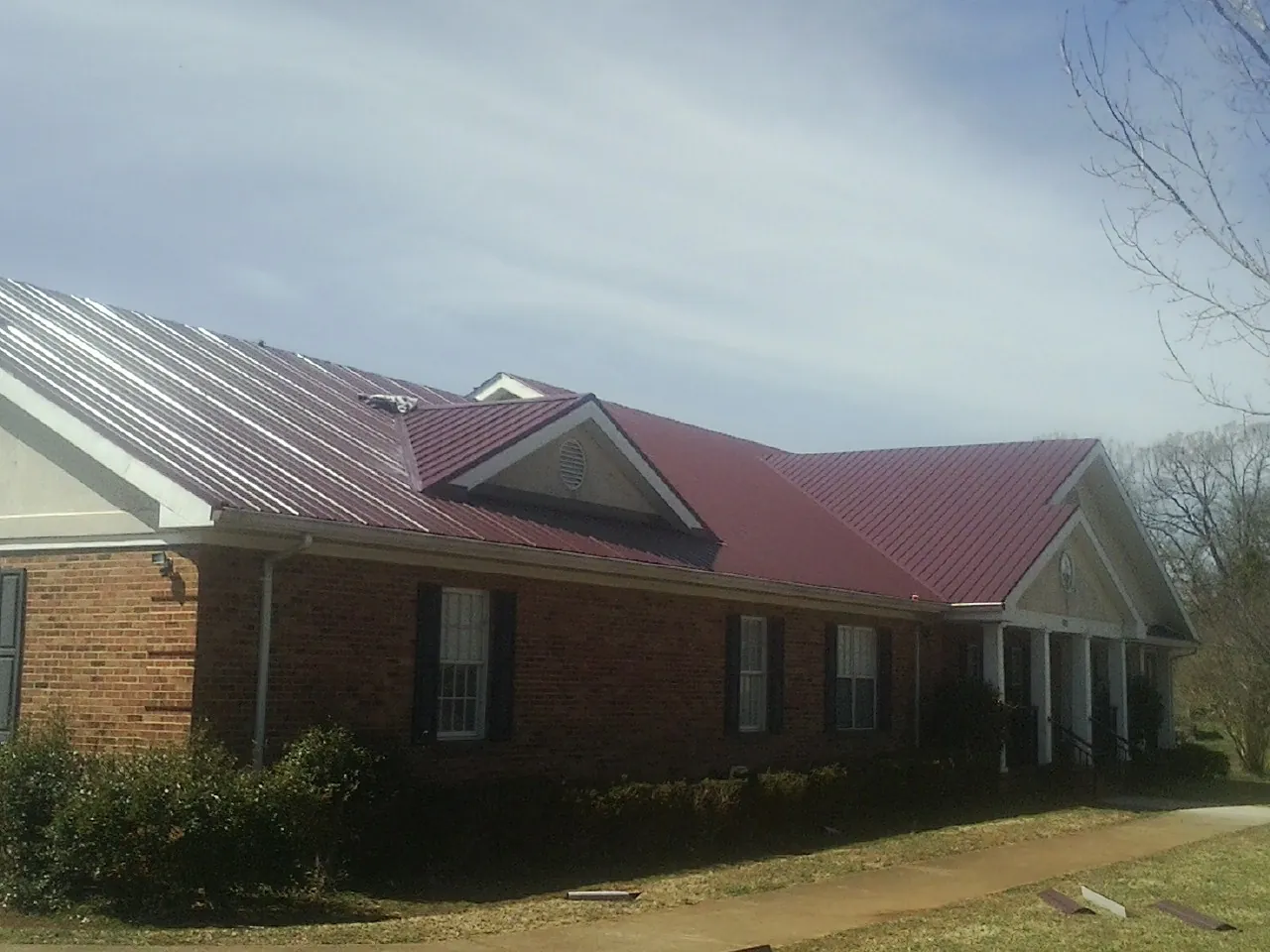 Red metal roof with gabled entries on a long brick building, from a Hail Damage Roof Repair job in Lake Mary