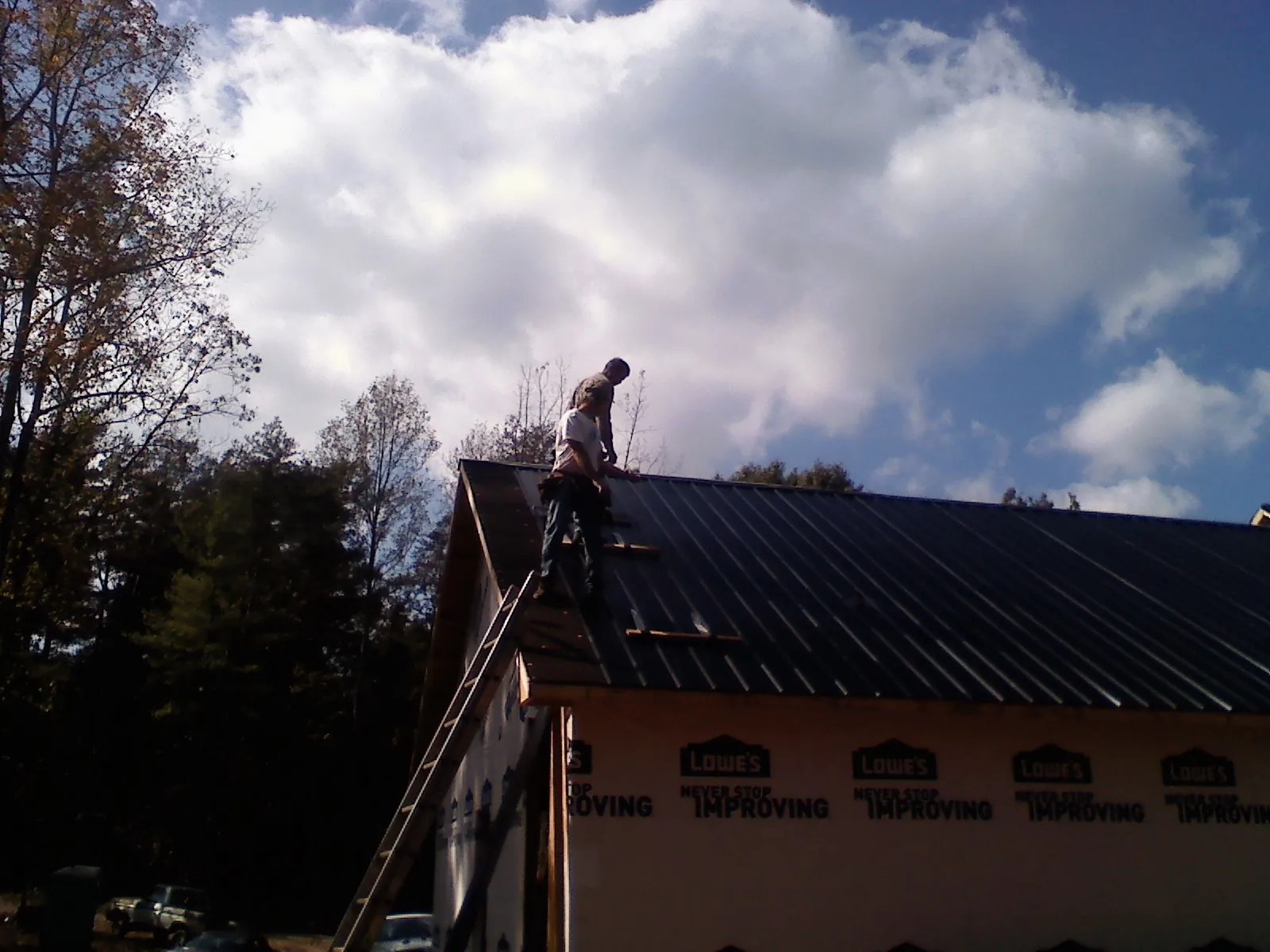 Roofer fastening dark metal panels high against a cloudy sky, from a Roof Inspection job in Lake Mary