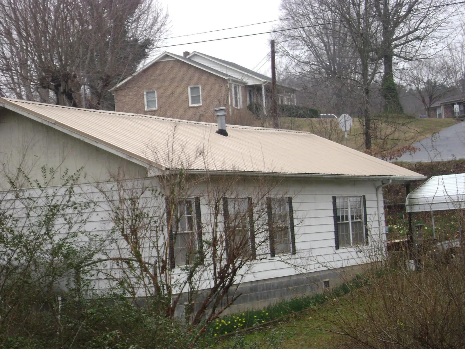 Tan metal roof on a white sided house set into a hillside — Commercial Roofing by Roofing Brothers in Lake Mary